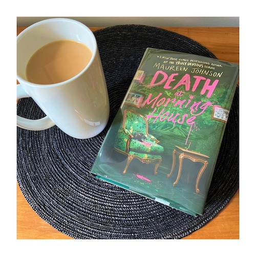 Photo of the book Death at Morning House on top of a round black placement with a cup of tea