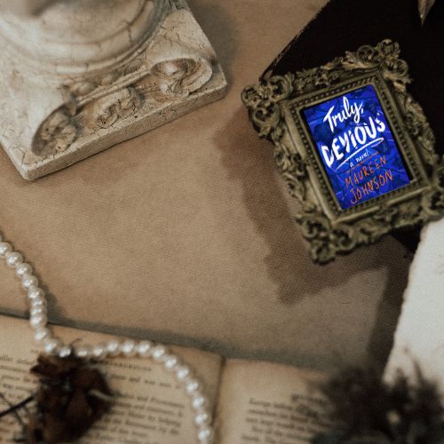 Photo of Truly Devious next to a marble bust, a string of pearls and a book